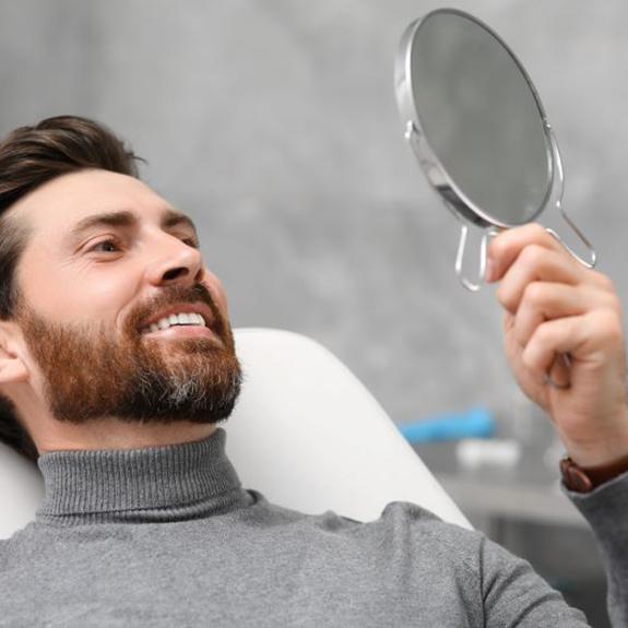 Dental patient holding mirror and looking at his smile