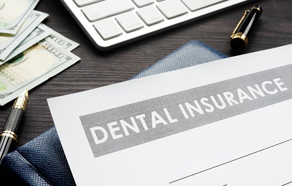 Dental insurance paperwork lying on table with money, laptop, and pens