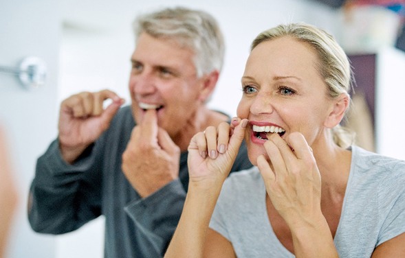 Senior couple smiling while flossing their teeth