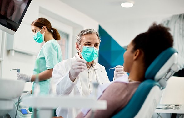 A smiling dentist with a face mask performing a dental checkup