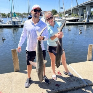 Two smiling people holding large fish on a dock