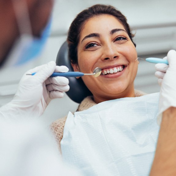 Woman in treatment chair smiling while dentist examines her teeth