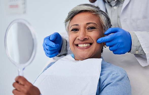 Woman smiling while holding handheld mirror in treatment chair