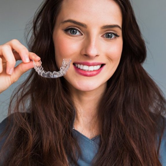 a woman smiling while holding SureSmile clear aligners