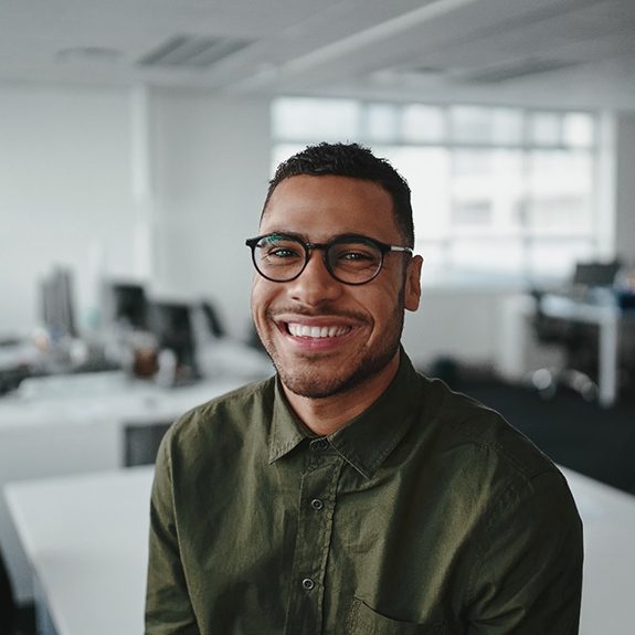 a smiling man sitting on a desk in an office